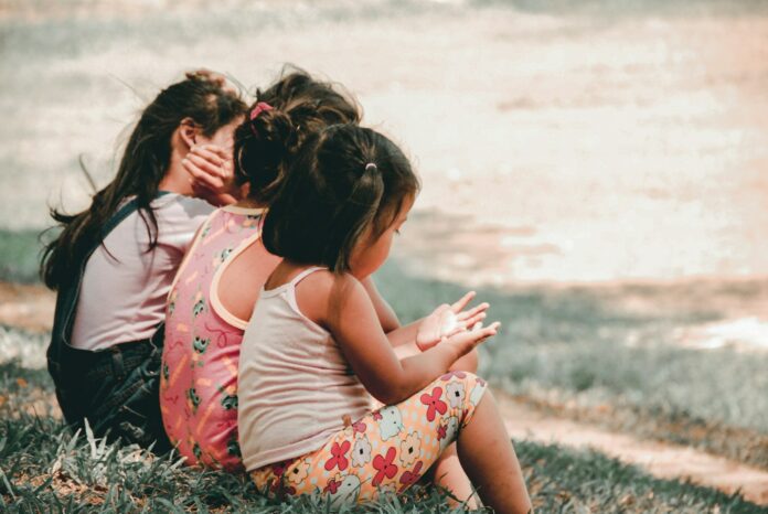 Photo by Charlein Gracia three children sitting on grass